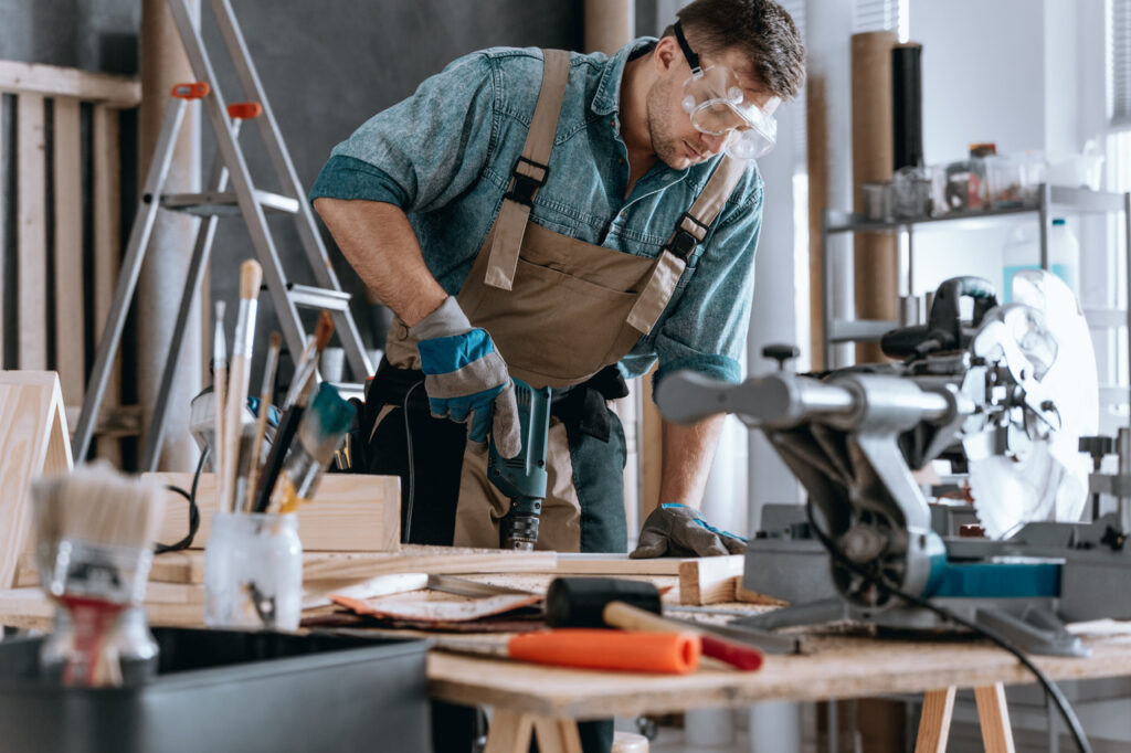 Young contractor drilling a hole in a piece of wood in his workshop