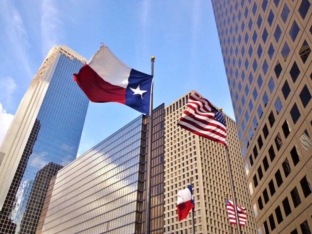 Low angle view of United States of America flag and Texas state flag in front of modern skyscrapers in downtown Houston (skyline / skyscrapers) on a summer day - Houston, Texas, USA